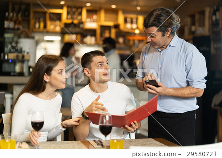Couple chooses food from the menu and asks the waiter Couple chooses food from the menu and asks the waiter 129580721
