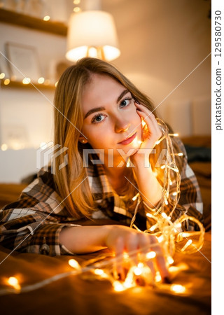 Woman Relaxing with String Lights in Cozy Atmosphere 129580730