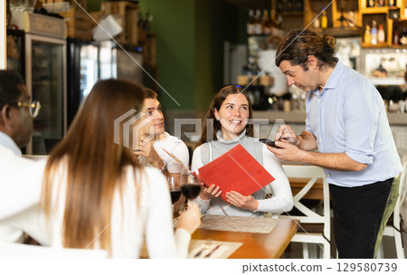 Man waiter writes down girls order. Employee serve couple clients in cafe 129580739