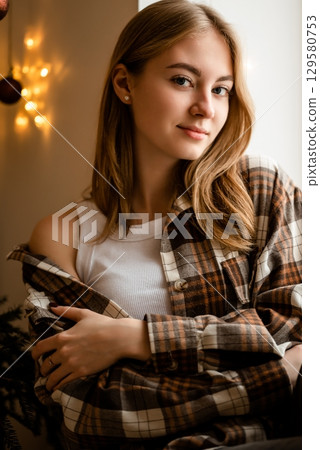 Young Woman Relaxing in Flannel Shirt by Window 129580753