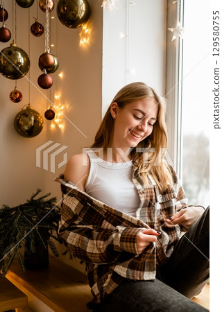Smiling Woman by Window Enjoying Christmas Decor 129580755