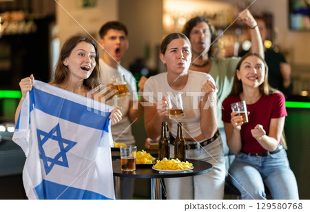 Group of friends cheer together for their favorite Israeli team in beer bar 129580768