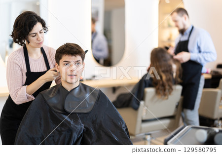 Young woman barbershop employee stands next to male client, discussing details of haircut 129580795