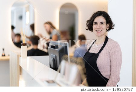 Female employee of barbershop stands near reception desk of salon, waits for visitors 129580797