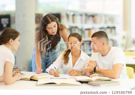 Group of student sits at table in library and studies, reads books and takes notes 129580799