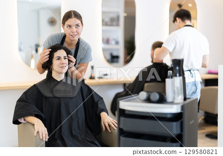 Young female hairdresser giving haircut to adult woman 129580821