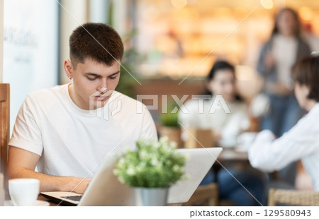 Young man with laptop drinking coffee Young man with laptop drinking coffee 129580943