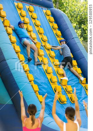 Cheerful man sliding down inflatable slide in outdoor amusement park Cheerful man sliding down inflatable slide in outdoor amusement park 129580955
