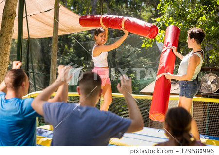 Young women having funny wrestling by inflatable logs in outdoor amusement playground 129580996