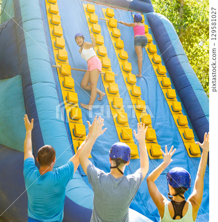 Women using sticks to reach top of slide in adventure park 129581027