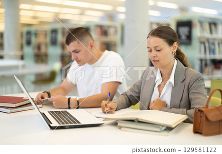 Guy and woman students reading books and working on laptop 129581122
