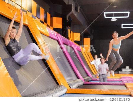 Middle-aged woman in sport clothes high jumping in trampoline arena Middle-aged woman in sport clothes high jumping in trampoline arena 129581170
