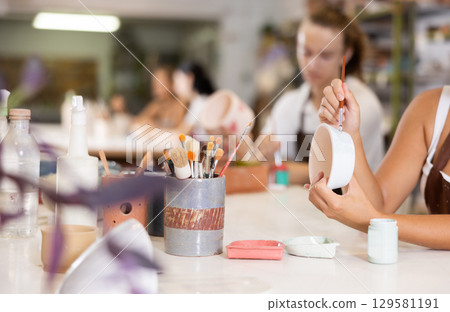 View of girl's hands painting ceramic bowl with brush 129581191