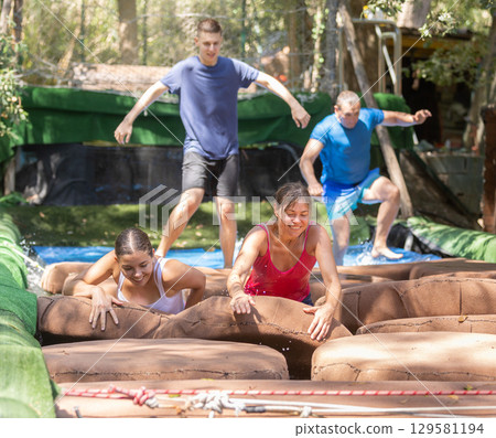 Men and women reaching finish of water obstacle course 129581194