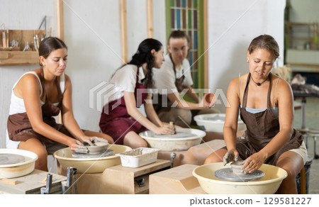 Young woman sits near potter wheel and makes clay crafts Young woman sits near potter wheel and makes clay crafts 129581227