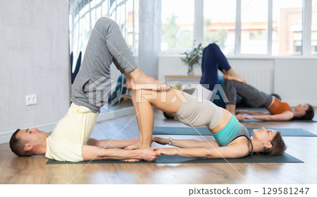 Lovers of active lifestyle perform pair yoga bridge and supported shoulderstand pose in gym Lovers of active lifestyle perform pair yoga bridge and supported shoulderstand pose in gym 129581247