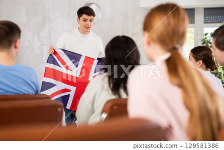 Young teacher holding flag of Great Britain in front of group of students 129581386