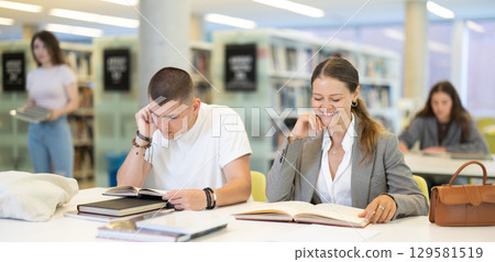Guy and woman students reading books in library 129581519