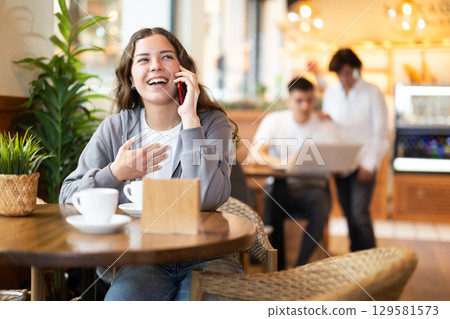 Girl in cafe drinks coffee and calling using mobile phone Girl in cafe drinks coffee and calling using mobile phone 129581573
