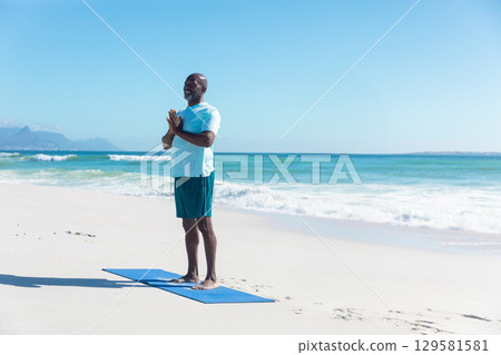 Senior African American man wearing sportswear holding pose on blue yoga mat on beach, copy space Senior African American man wearing sportswear holding pose on blue yoga mat on beach, copy space 129581581