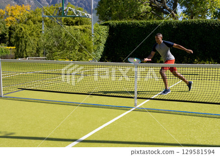 Male tennis player lunging with racket, hitting yellow ball above net on grass court, copy space 129581594