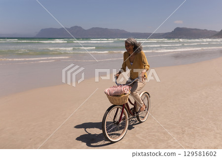 Middle-aged woman cycling along sandy beach on red cruiser bicycle with woven basket, copy space Middle-aged woman cycling along sandy beach on red cruiser bicycle with woven basket, copy space 129581602