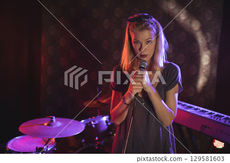 Female vocalist performing on small stage under colored spotlights with microphone and drum kit Female vocalist performing on small stage under colored spotlights with microphone and drum kit 129581603