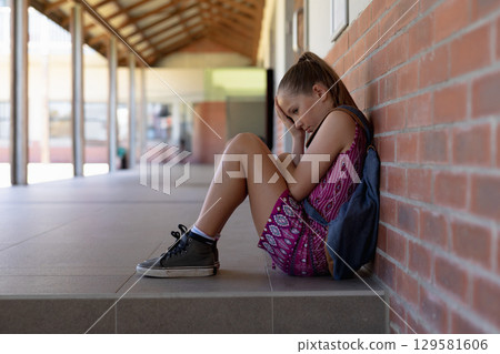 Child student sitting on tiled step at school corridor with backpack against brick wall, copy space 129581606