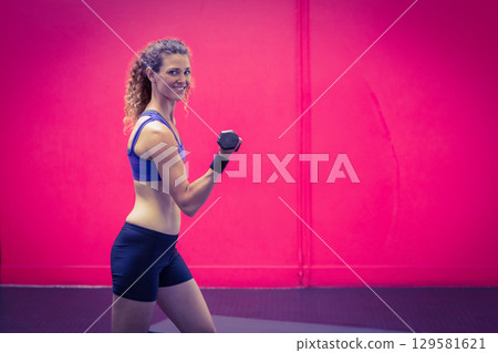 Woman performing bicep curl with hexagonal dumbbell on gym mat wearing sportswear, copy space Woman performing bicep curl with hexagonal dumbbell on gym mat wearing sportswear, copy space 129581621
