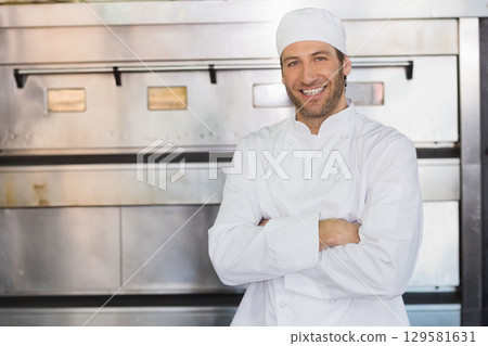 Male chef wearing white coat and skull cap showcasing steel oven in restaurant kitchen, copy space 129581631
