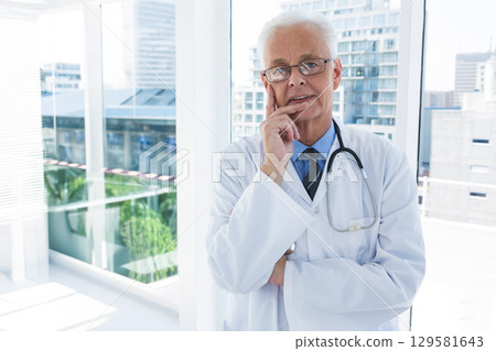 Senior male doctor wearing white coat and stethoscope, leaning by windows, viewing city, copy space Senior male doctor wearing white coat and stethoscope, leaning by windows, viewing city, copy space 129581643