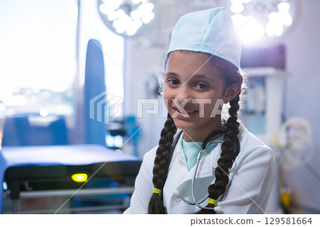 Preteen Asian girl standing in surgical suite wearing cap and coat holding stethoscope, copy space Preteen Asian girl standing in surgical suite wearing cap and coat holding stethoscope, copy space 129581664