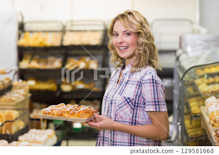 Female bakery clerk wearing plaid shirt presenting tray of braided buns inside bakery shop Female bakery clerk wearing plaid shirt presenting tray of braided buns inside bakery shop 129581668