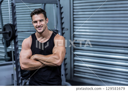 Muscular man wearing black tank top standing at gym by squat rack with plates, copy space 129581679