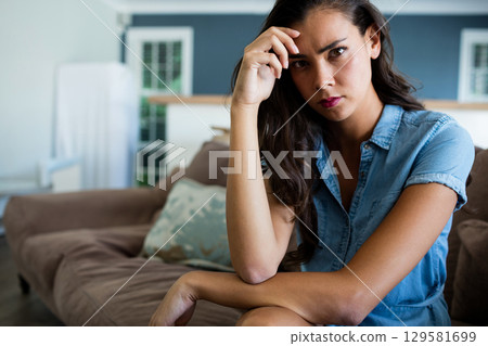 Woman in denim dress sitting in living room on sofa holding head near cushion, copy space 129581699
