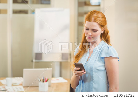 Red-haired woman standing in meeting room checking smartphone with laptop and flipchart, copy space Red-haired woman standing in meeting room checking smartphone with laptop and flipchart, copy space 129581722
