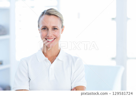 Mid adult woman standing with arms crossed smiling in bright office wearing white polo shirt Mid adult woman standing with arms crossed smiling in bright office wearing white polo shirt 129581724