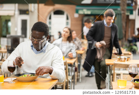 African man sits on terrace of a restaurant and eats 129581733