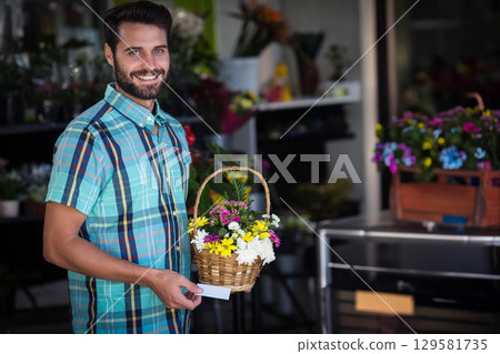 Man in late twenties standing inside flower shop holding wicker flower basket and blank card 129581735