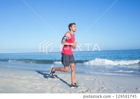 Man jogging along sandy beach wearing red tank top and black running shoes with smartphone armband Man jogging along sandy beach wearing red tank top and black running shoes with smartphone armband 129581745