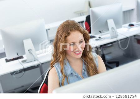 Woman wearing sleeveless denim shirt sitting in task chair using desktop monitor at computer lab Woman wearing sleeveless denim shirt sitting in task chair using desktop monitor at computer lab 129581754