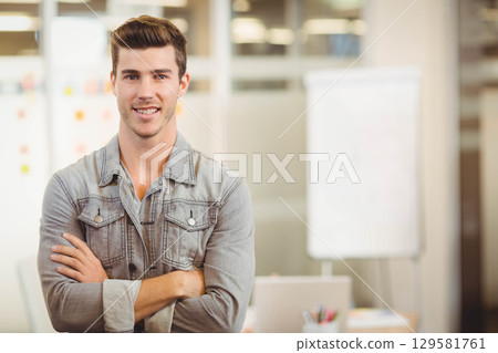 Man wearing gray denim shirt standing with arms crossed in modern office near whiteboard and laptop Man wearing gray denim shirt standing with arms crossed in modern office near whiteboard and laptop 129581761