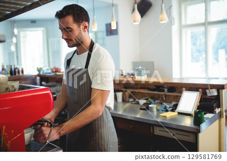 Male barista operating red espresso machine behind wooden counter in coffee shop with knock box Male barista operating red espresso machine behind wooden counter in coffee shop with knock box 129581769