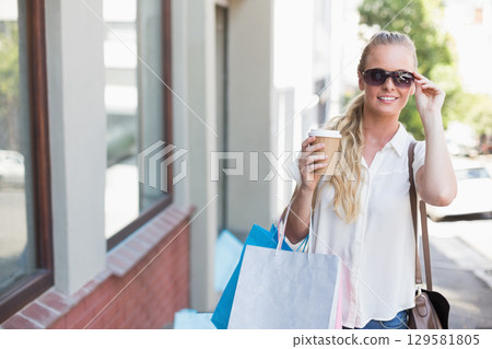 Woman in her late twenties standing outside storefront holding coffee cup and bags, copy space Woman in her late twenties standing outside storefront holding coffee cup and bags, copy space 129581805