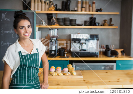 Female barista wearing striped apron handling pastry board and espresso machine at cafe, copy space Female barista wearing striped apron handling pastry board and espresso machine at cafe, copy space 129581820