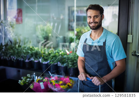 Man wearing apron arranging bouquets on wheeled cart in flower shop with glass panels, copy space 129581835