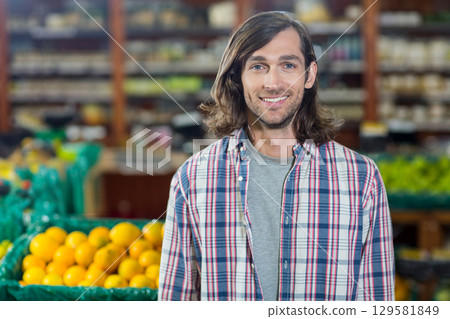 Man in his thirties standing in supermarket produce inspecting yellow oranges in green crates Man in his thirties standing in supermarket produce inspecting yellow oranges in green crates 129581849