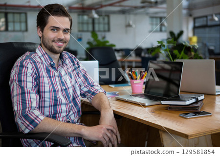 Male office worker sitting at desk in open-plan office using laptop, smartphone, copy space Male office worker sitting at desk in open-plan office using laptop, smartphone, copy space 129581854