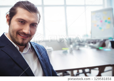 Businessman sitting at conference table by windows smiling near whiteboard sticky notes copy space 129581858