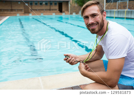 Male swim coach crouching at outdoor lap pool edge holding neon cord stopwatch, copy space Male swim coach crouching at outdoor lap pool edge holding neon cord stopwatch, copy space 129581873